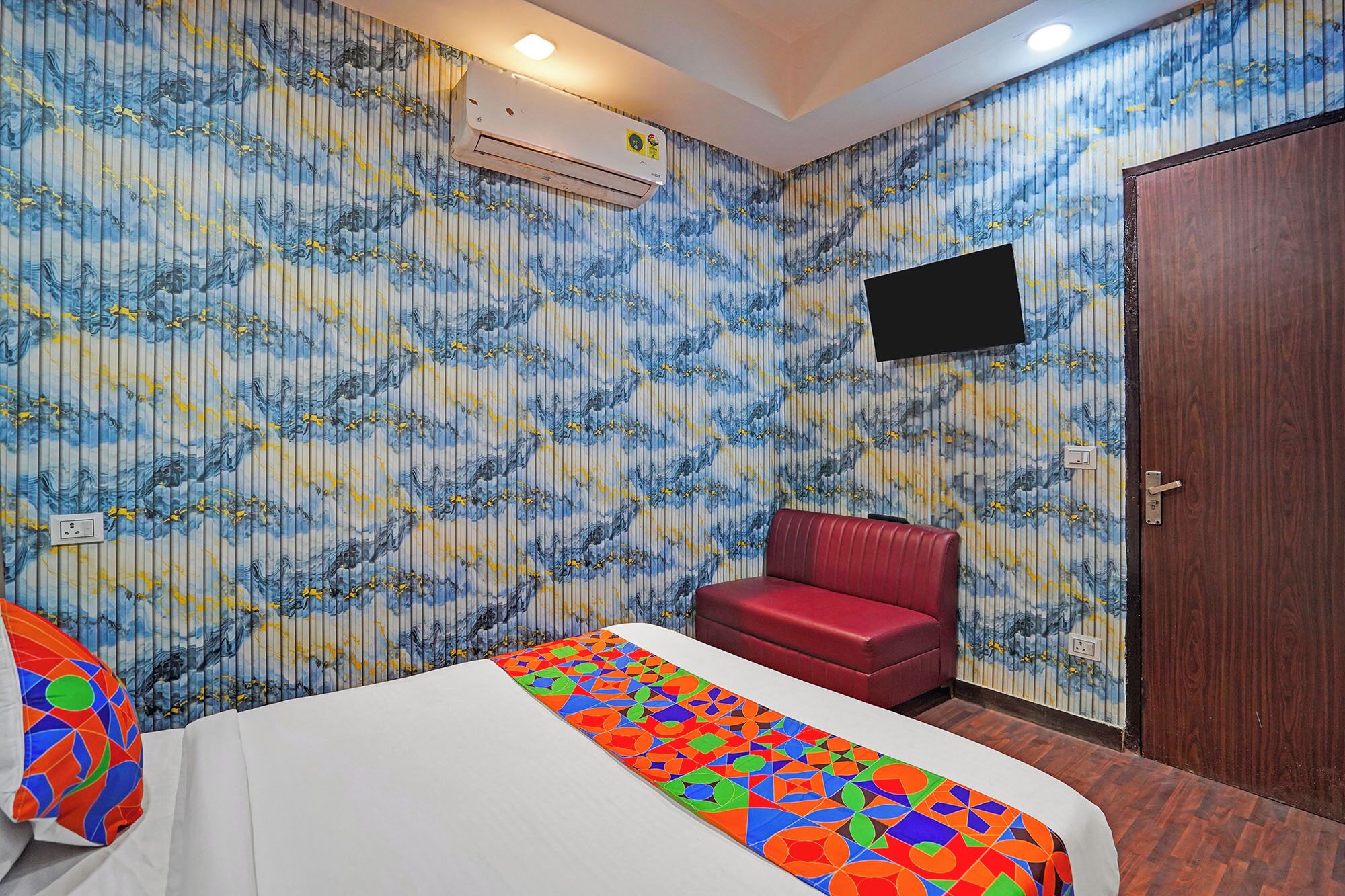 Een hotelkamer met een bed, een rode stoel, een aan de muur bevestigde televisie en een airconditioning.