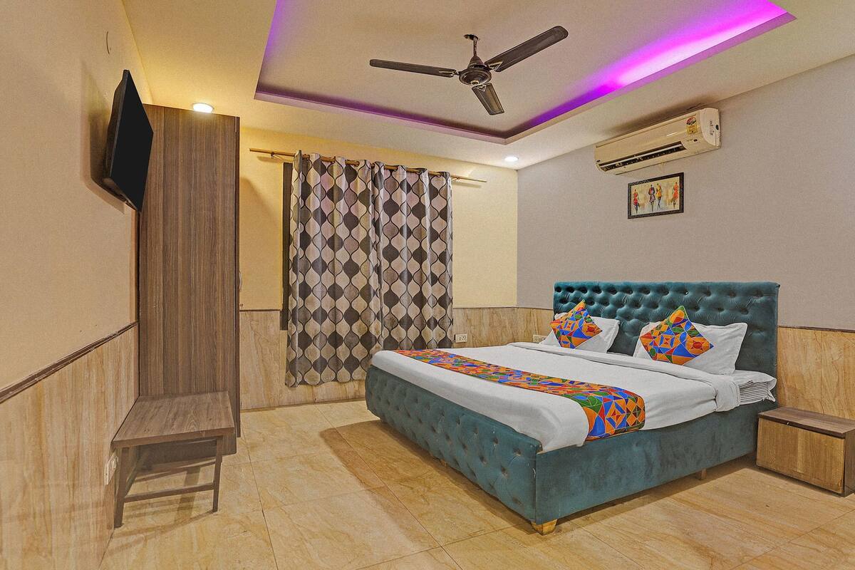 A bedroom with a tufted headboard, a bed with colorful pillows, a ceiling fan, an air conditioning unit, and a patterned curtain.