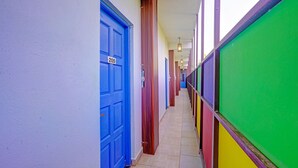 A narrow hallway with colorful doors and walls, leading to a bright room with a tiled floor. - Via Padma (Morjim)