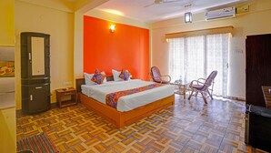 A hotel room with a large bed, a ceiling fan, an air conditioning unit, a wooden floor, a window with curtains, and a small table with chairs. - Via Padma (Morjim)