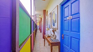 A hallway with colorful walls, a blue door labeled 202, and a table with a vase and books. - Via Padma (Morjim)