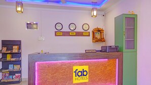 A hotel reception desk with a 'fab hotels' sign, clocks displaying different times, and a 'Reception' sign above the desk. - Via Padma (Morjim)