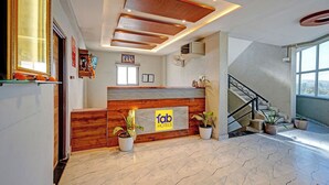 A hotel reception area with a wooden reception desk, potted plants, and a staircase leading to an upper floor. - Fabhotel Pearl Inn (Rajgurunagar)