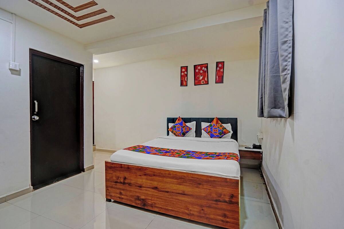 A hotel room with a wooden bed, white walls, a dark door, and a ceiling with wooden beams.
