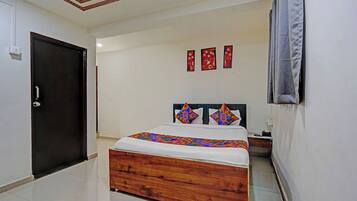 Una habitación de hotel con una cama de madera, paredes blancas, una puerta oscura y un techo con vigas de madera.