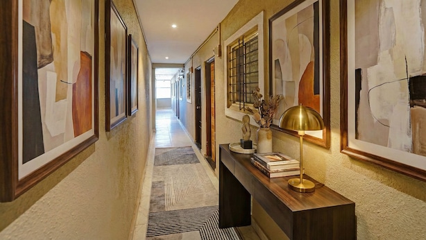 A hallway with abstract paintings, a desk with a lamp, and a patterned rug. - Fabhotel Pearl Inn (Rajgurunagar)