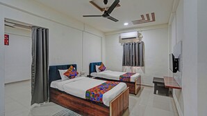 A hotel room with two beds, a ceiling fan, an air conditioning unit, a small desk, and a window with curtains. - Fabhotel Pearl Inn (Rajgurunagar)