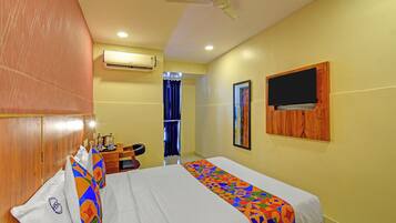 A hotel room with a bed, a desk, an air conditioner, a ceiling fan, and a TV mounted on the wall.
