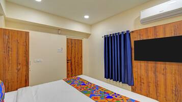 A hotel room with a bed, a wooden wardrobe, a blue curtain, an air conditioning unit, and a wall-mounted TV.
