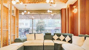 A modern living room with a sectional sofa, decorative wooden panels, and a view of the cityscape through large windows. - Fabhotel Raj Niwas (New Delhi)