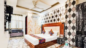 A hotel room with a marble floor, a bed with a wooden headboard, a bedside table with a bottle and glasses, and a mirror on the wall. - Fabhotel Raj Niwas (New Delhi)