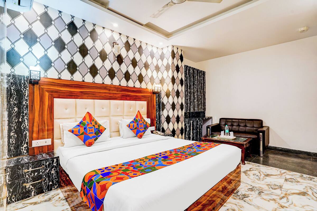 A hotel room with a large bed, a wooden headboard, a patterned wall, a small table with a bottle, and a leather armchair.