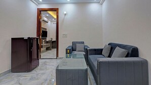 A modern living room with a sofa, a coffee table, and a TV. There is a kitchen visible through an open doorway. - FabHotel Premier Stays - 800m from Artemis Hospitals Gurgaon (Gurugram)