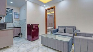 A compact living space with a kitchenette, a glass-top coffee table, a sofa with patterned cushions, and a wardrobe. - FabHotel Premier Stays - 800m from Artemis Hospitals Gurgaon (Gurugram)