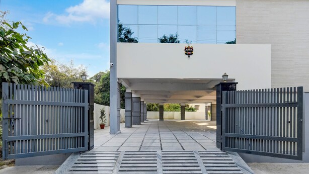 A modern building entrance with a gated driveway, a small potted plant, and a decorative mask above the door.