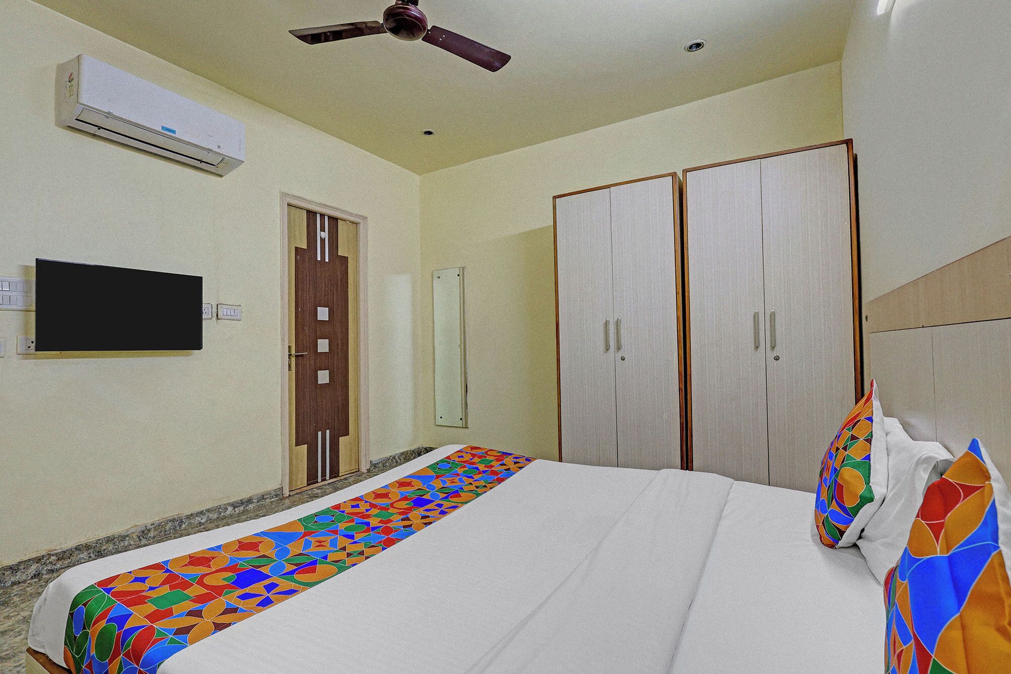 A hotel room with a bed, a ceiling fan, an air conditioning unit, a TV, and a wardrobe.