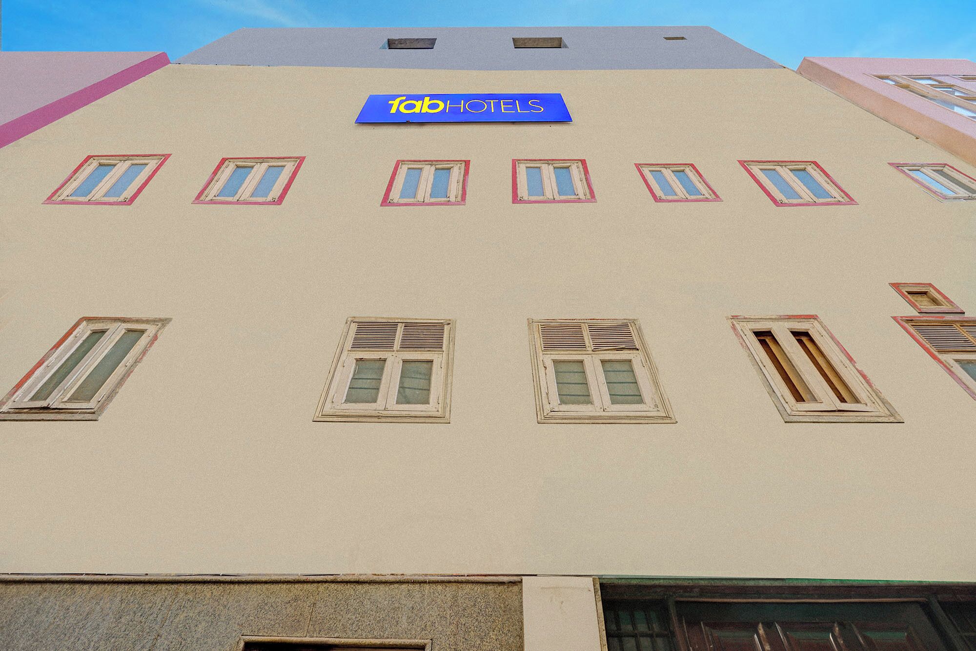 A building with a 'fabHOTELS' sign, multiple windows with shutters, and a flat facade.