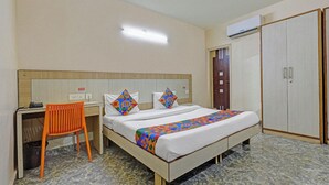 Ein Hotelzimmer mit einem Bett, einem Schreibtisch, einem orangefarbenen Sessel, einem Kleiderschrank und einer Klimaanlage.