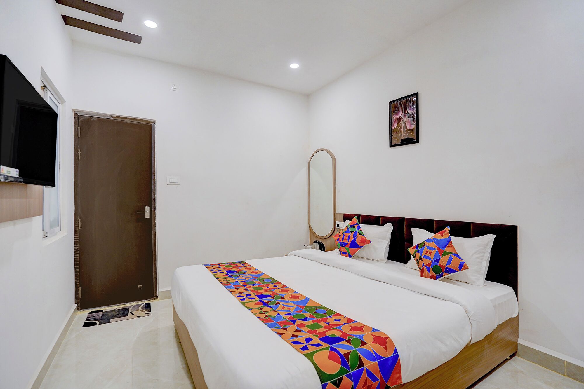 A hotel room with a bed, a mirror, a TV, and a door.