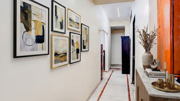 A hallway with framed abstract art, a marble floor, and a wooden cabinet with decorative items. - Fabhotel Sarala Residency (Noida)