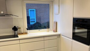 Eine moderne Küche mit weißen Schränken, einem eingebauten Ofen und einem Fenster mit Blick auf ein Backsteingebäude.