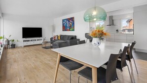 Ein modernes Wohnzimmer mit Essbereich, einem Flachbildfernseher, einer Couch und einer Küche im Hintergrund.