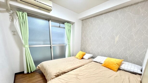 Ein Schlafzimmer mit zwei Betten, einem Fenster mit Vorhängen, einer Klimaanlage und einer Wand mit Muster.