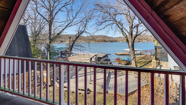 Une vue depuis un balcon donnant sur un lac où sont amarrés des bateaux, avec une terrasse en bois et un ciel dégagé.