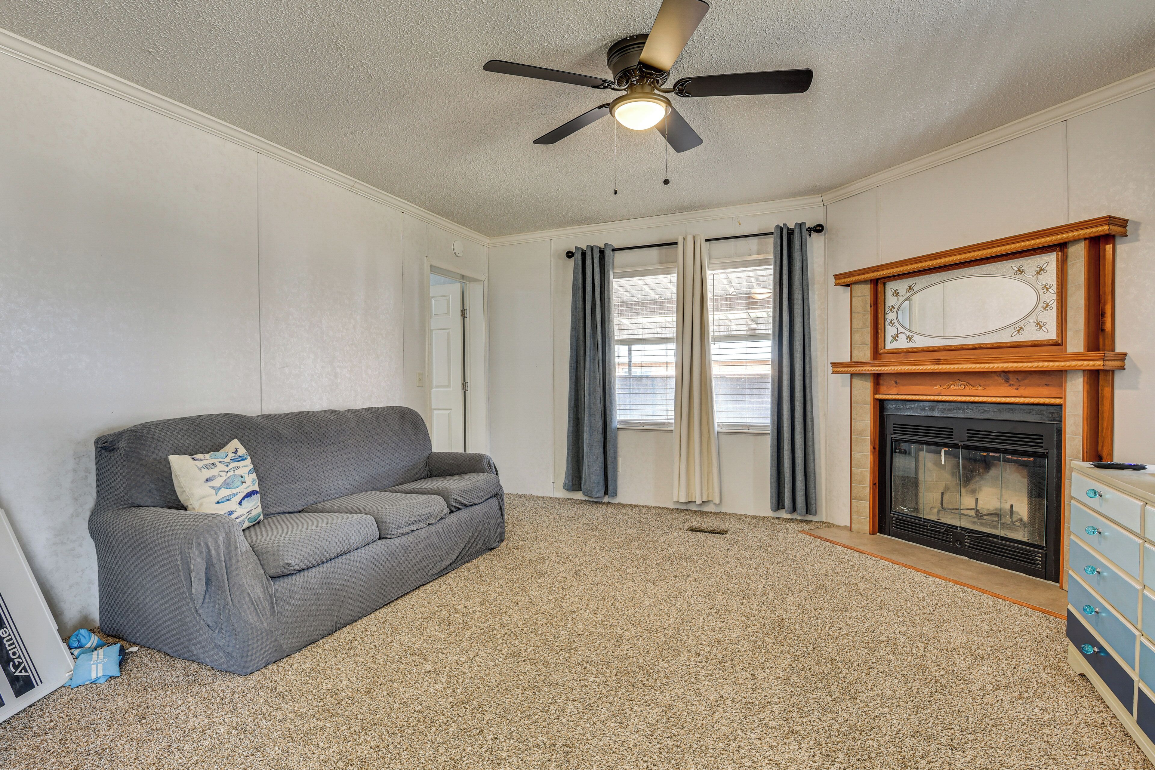 A living room with a gray sofa, a ceiling fan, a fireplace, and a dresser.