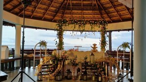 Un espacio al aire libre cubierto con techo de paja, decorado con flores y faroles, con vistas a un cuerpo de agua.