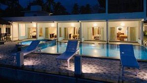 Un hotel con piscina, varias habitaciones con puertas de vidrio y sillones de descanso.