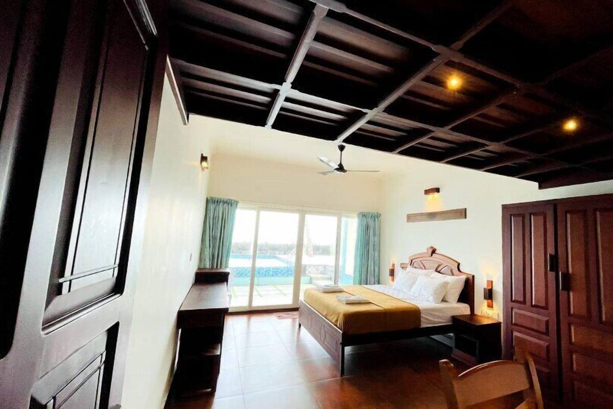 A bedroom with a bed, a desk, a chair, a wardrobe, and a view of the outside.