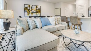 A modern living room with a sectional sofa, a round coffee table, and a dining area with bar stools. - 8 Mi to Dtwn Pensacola: Modern Escape w/ Patio! (Pensacola)
