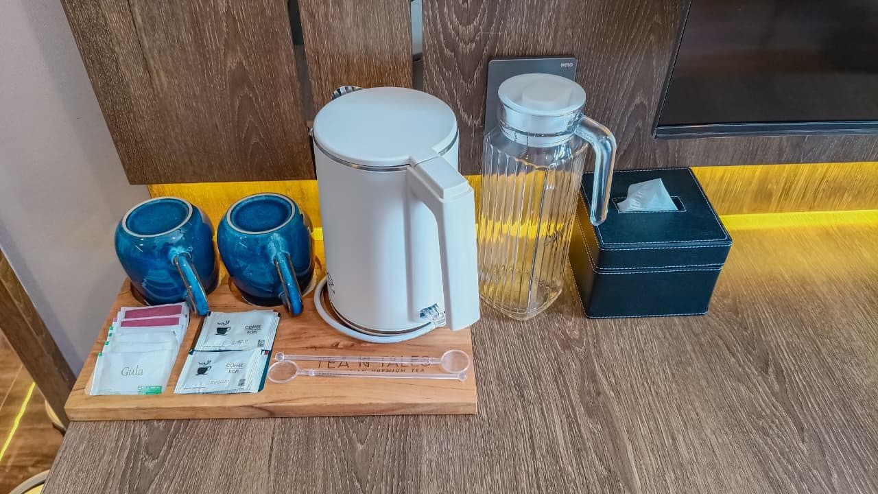 Een koffiehoek met een koffiezetapparaat, twee blauwe mokken, een glazen pot, een zakdoekendoos en theezakjes op een houten dienblad.