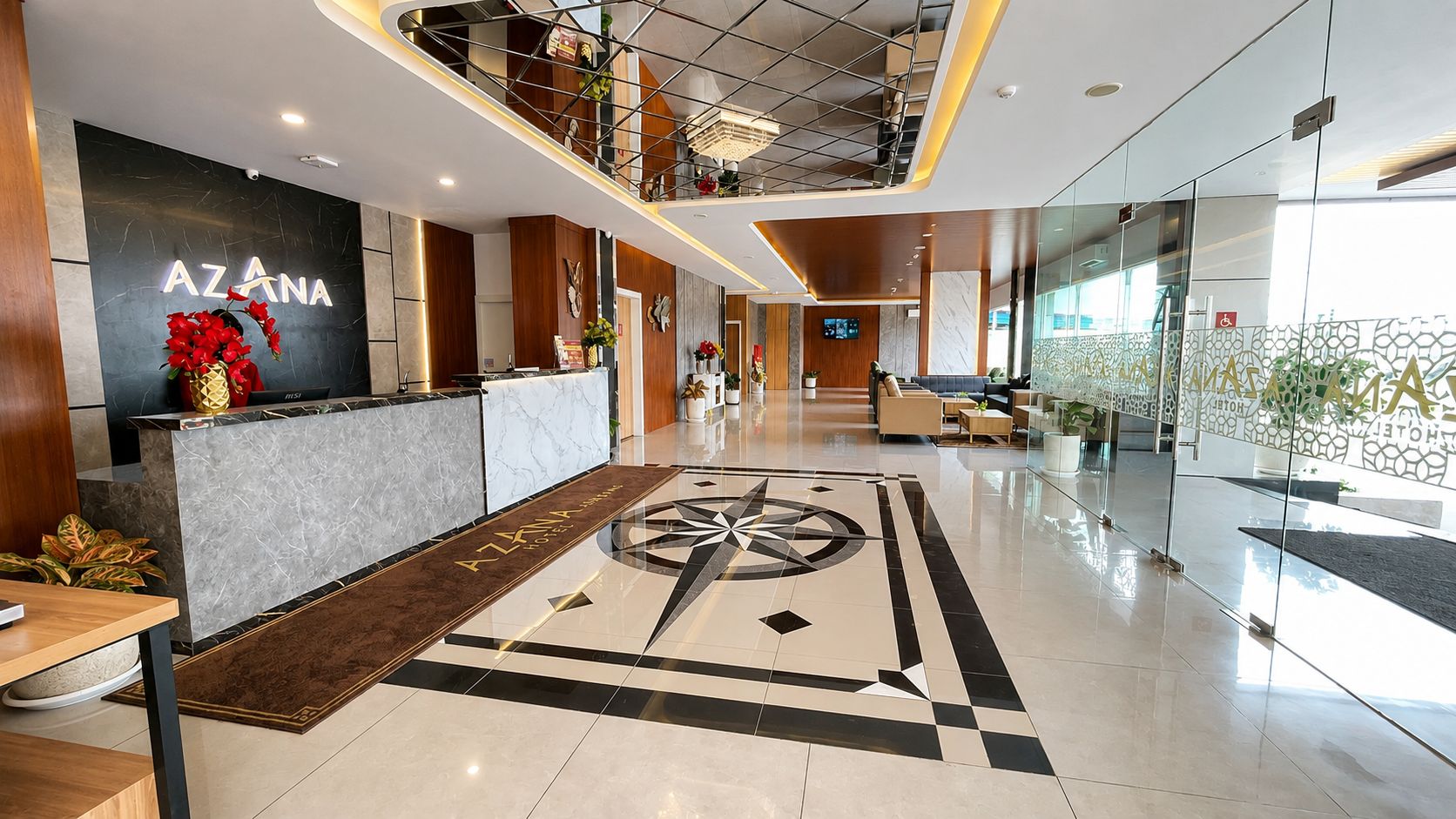 Eine Hotelhalle mit einer Rezeption, einem großen geometrischen Bodenmuster und einer Treppe, die in einen oberen Bereich führt.