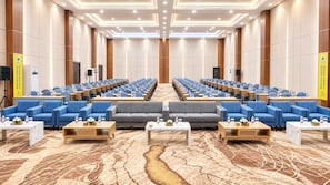 A conference room with rows of tables and chairs, a stage, and a carpeted floor. - Azana Style Hotel Jombang (Peterongan)