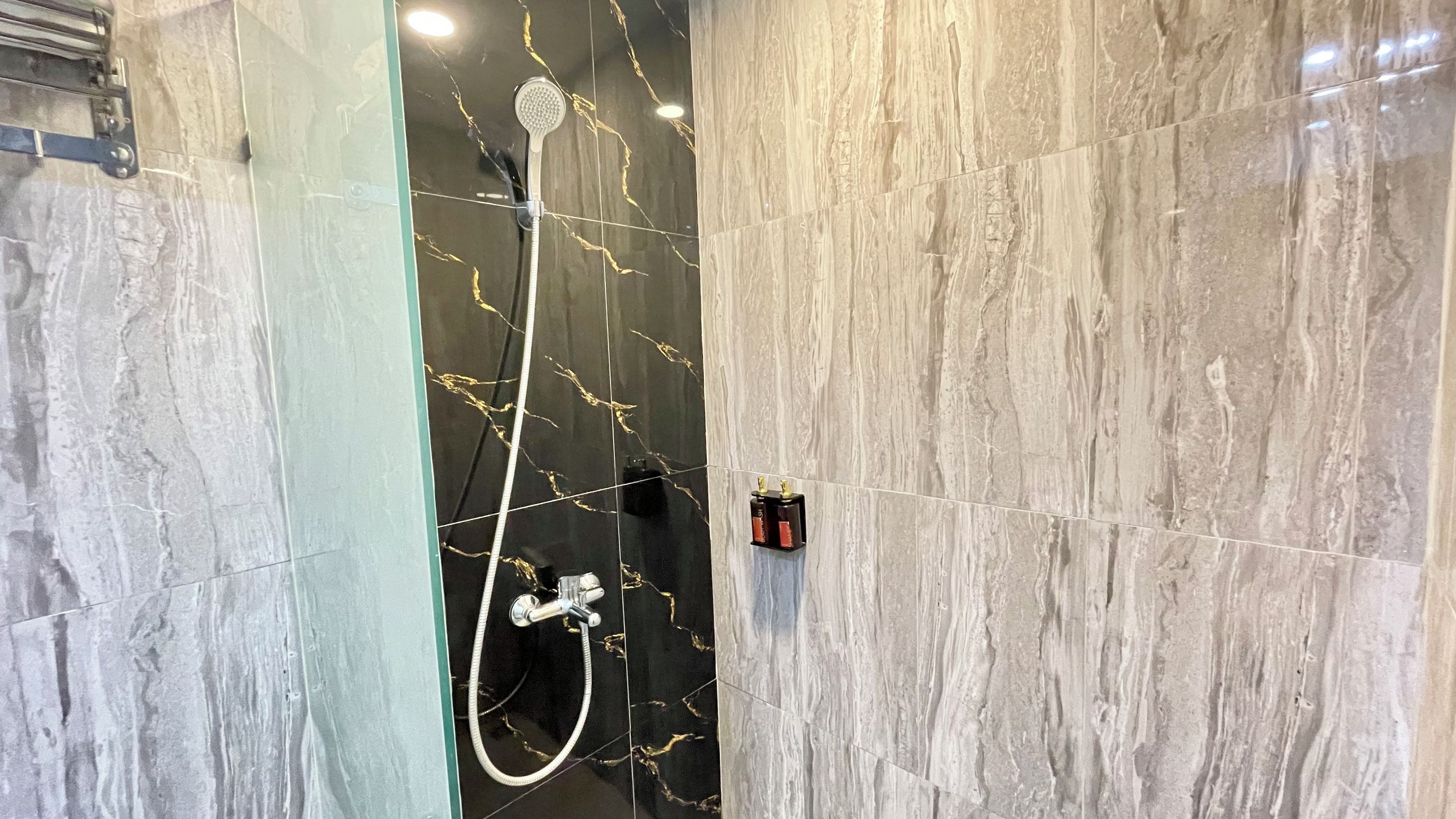 Ein Badezimmer mit Dusche, Marmorwänden und einem sichtbaren Warmwasserbereiter.