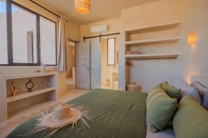A bedroom with a large bed, a window with curtains, a shelf with decorative items, and a wall-mounted shelf with towels. - Lalla Essaouira - Villa Koulchi, 10 bedroom, until 28 peop with staff (Essaouira)