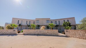 Un edificio moderno con facciata in pietra, numerose finestre e palme sullo sfondo.