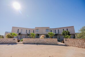 A modern building with a stone facade, multiple windows, and palm trees in the foreground. - Lalla Essaouira - Villa Koulchi, 10 bedroom, until 28 peop with staff (Essaouira)