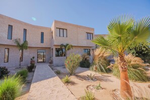 A modern building with a flat roof, large windows, and a paved entrance area with a pathway leading to the door. - Lalla Essaouira - Villa Koulchi, 10 bedroom, until 28 peop with staff (Essaouira)