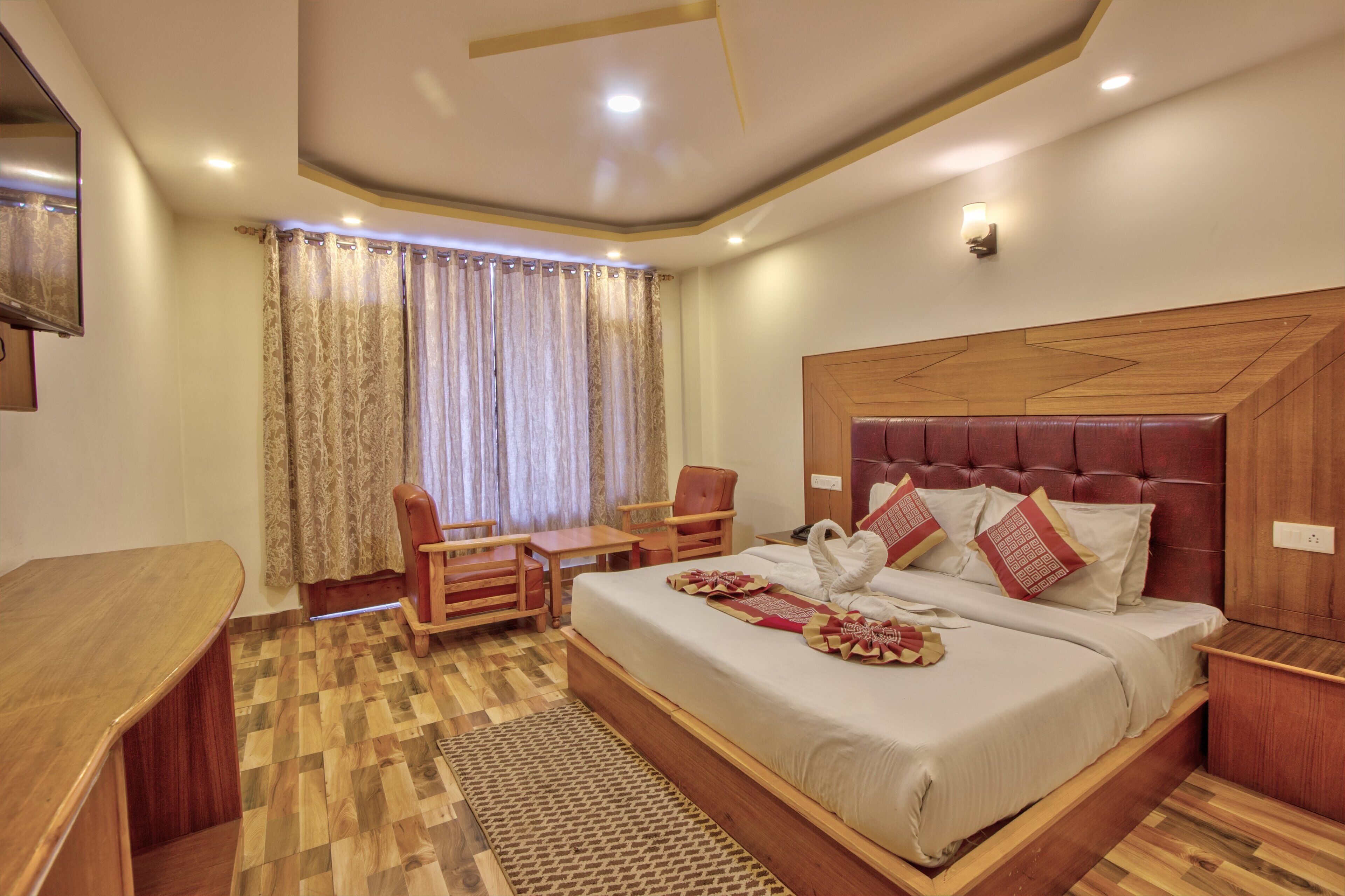 A hotel room with a wooden bed, a desk, a chair, and a large window with curtains.