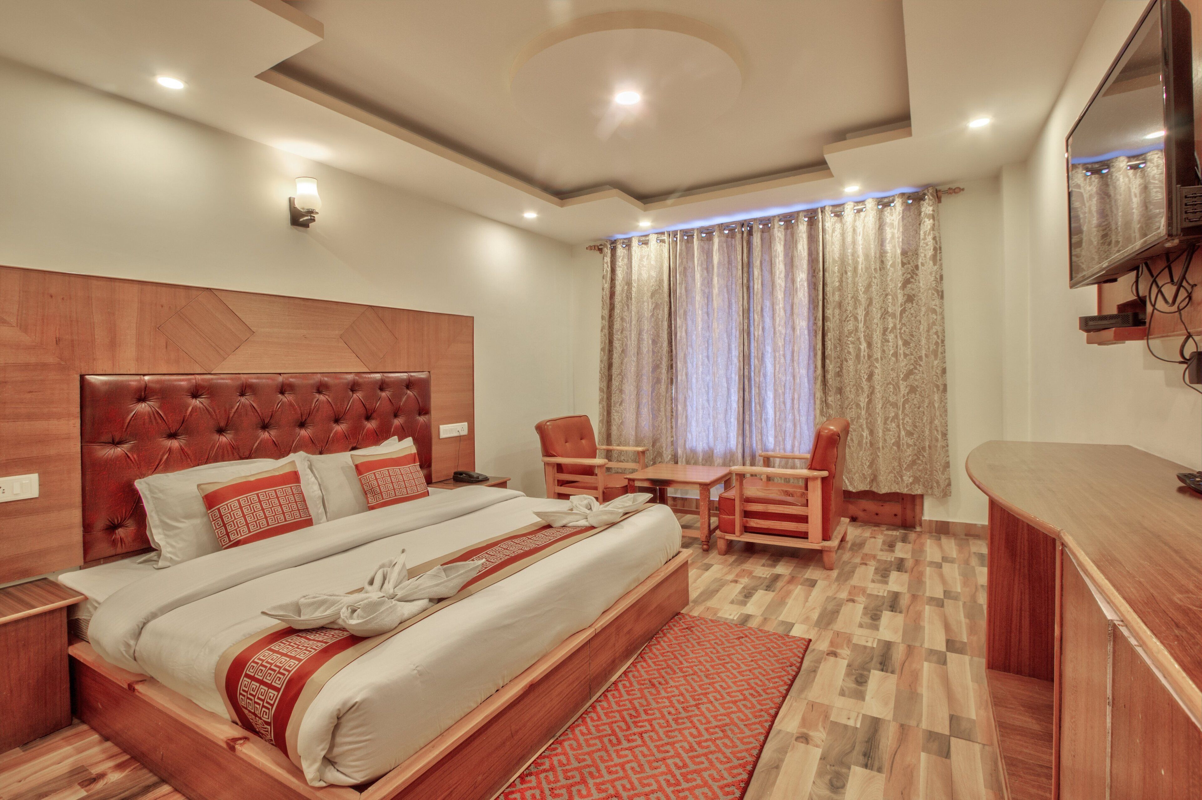 A hotel room with a large bed, a wooden headboard, a desk, and a TV mounted on the wall.