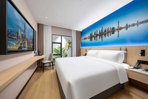 Quarto de hotel com cama grande, escrivaninha, cadeira, televisão e um mural com vista urbana na parede.
