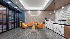 A modern lobby with a reception desk, two orange chairs, a small table, and a potted plant. - Pengcheng Lijing Hotel  (Shenzhen)