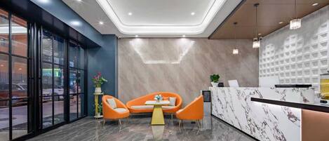 Un hall d’entrée moderne avec un comptoir d’accueil, deux fauteuils orange, une petite table et une plante en pot.