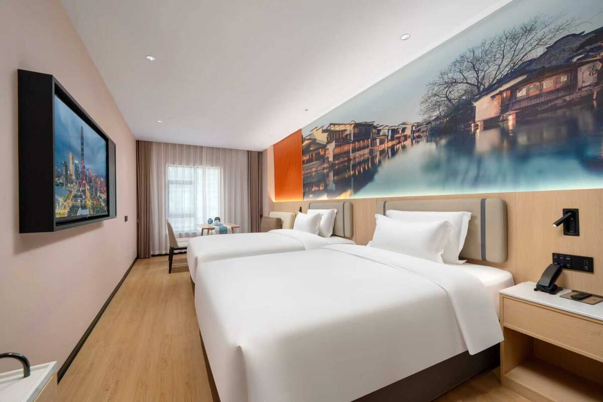 A hotel room with two beds, a desk, a chair, and a large wall painting.