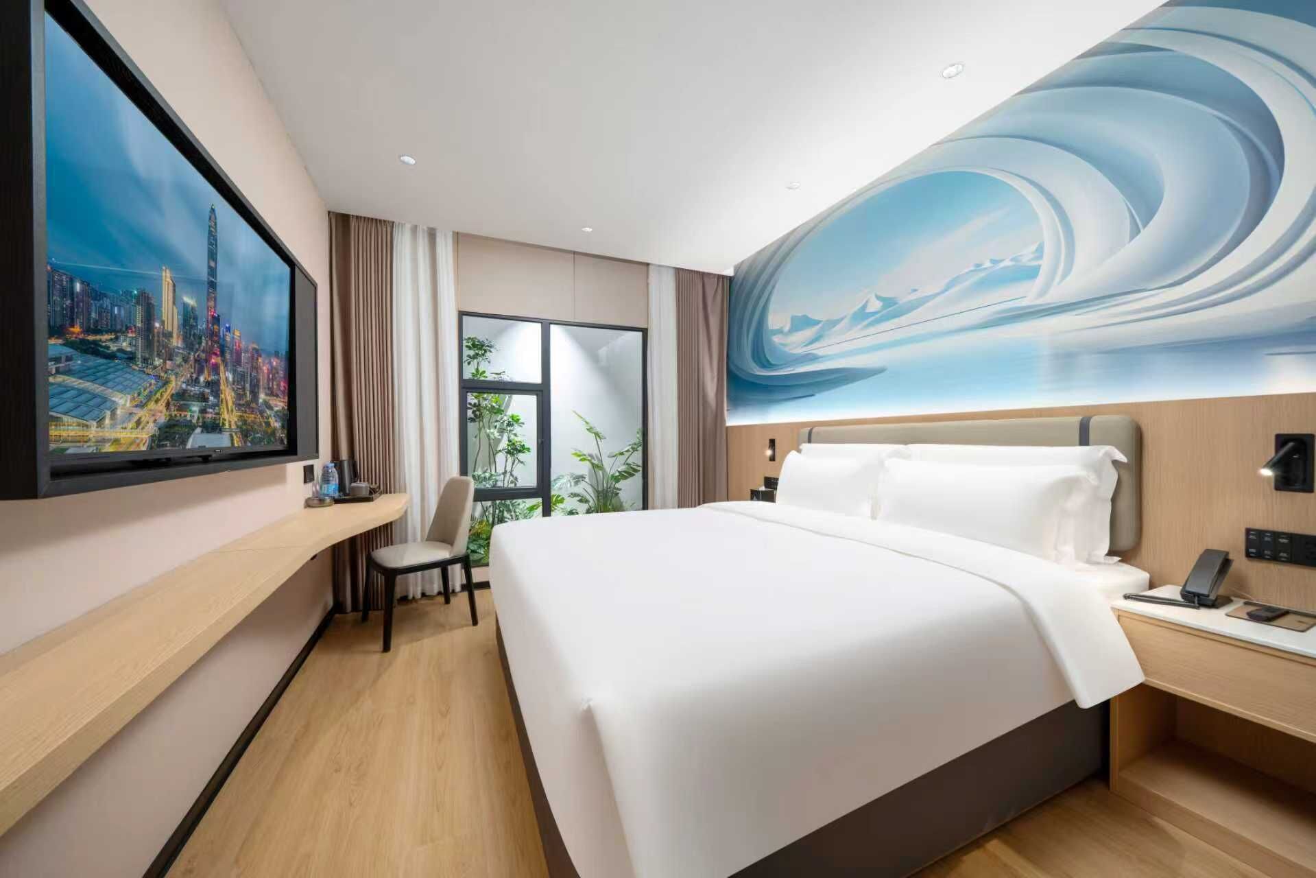 A modern hotel room with a large bed, a desk, and a TV displaying a cityscape.