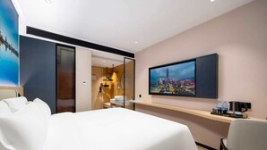 A hotel room with a large bed, a desk with a chair, a TV mounted on the wall, and a bathroom visible through an open door. - Pengcheng Lijing Hotel  (Shenzhen)