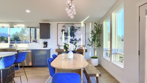 A modern kitchen with a dining area, large windows, and a decorative light fixture. - The Hills Edge - Stunning Views, Hot Tub & Games (Mariposa)